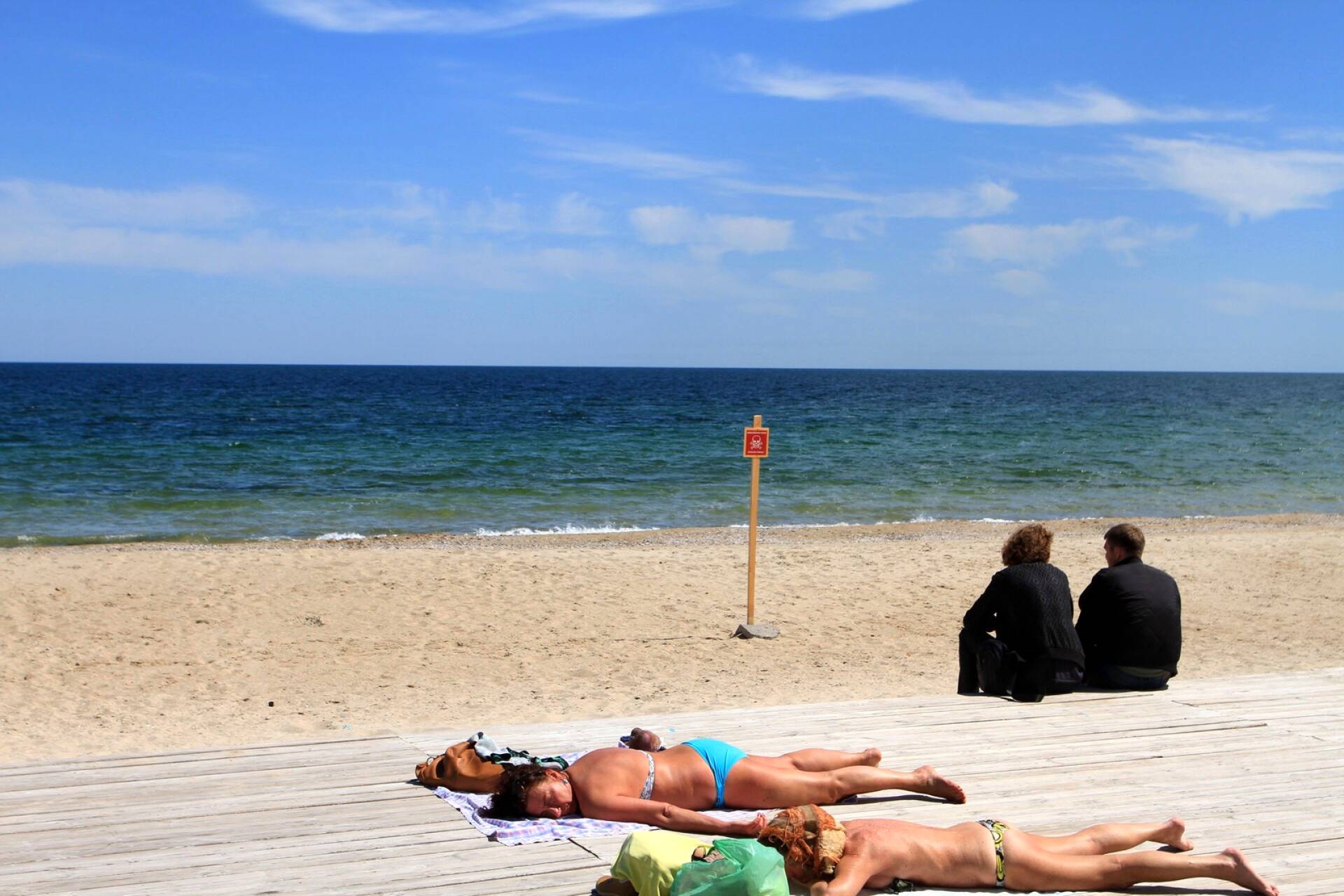 Ihmiset ottivat aurinkoa rannalla Odessassa. Taustalla olevassa kyltissä varoitetaan miinoista.