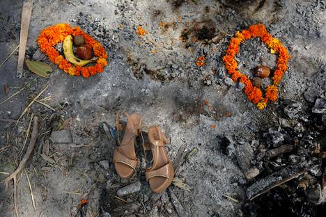 Koronaan menehtyneen naisen omaiset asettivat kengät, kukkaseppeleitä sekä hedelmiä kohtaan, jossa hänet tuhkattiin delhiläisessä krematoriossa perjantaina. Esineiden asettelu on osa hautajaisrituaalia.