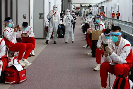 Suojapukuiset viranomaiset kävelivät Kiinan olympiajoukkueen jäsenten ohi Naritan lentokentälllä Tokiossa.