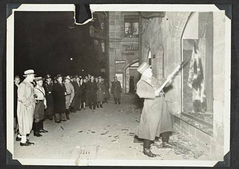 Tässä aiemmin julkaisemattomassa kuvassa näkyy, kuinka natsit tuhoavat juutalaisten liikkeitä ilmeisesti Fürthin kaupungissa Kristalliyönä 1938. Siviilit seuraavat tekoja sivusta.