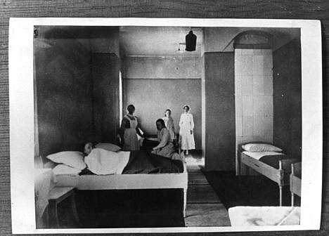 Vanhassa valokuvassa näkyy käytävästä lämmitettävä kaakeliuuni. Potilaiden vuoteisiin saatiin tarvittaessa laidat ja verkko päälle.