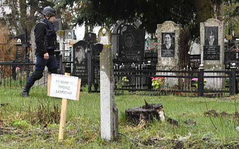 Miinoja, pääsy kielletty -kyltti Makarivin hautausmaalla ja sotilas tutkimassa mahdollisia miinoja Makarovin hautausmaalla ennen pääsiäisen vierailuja haudoilla.