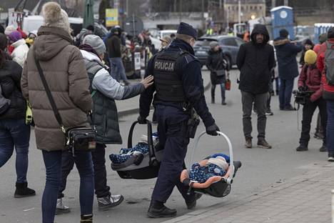 Medykan raja-asemalla Puolassa pakolaisten määrä lisääntyy. Poliisi kuljettaa kahta sylivauvaa.