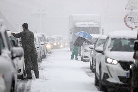 Kuljettajat puhdistavat autojaan lumesta, kun liikenne on jumiutunut Attiki Odos -moottoritiellä.