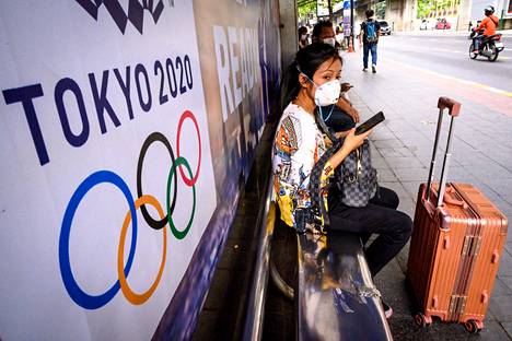 Nainen Tokion olympialaisetn mainosplakaatin edustalla Bangkokissa.